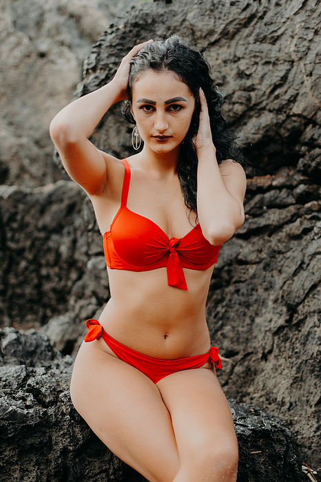 young woman posing in a red bikini on the rocks of a beach