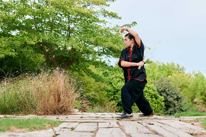 Woman training kung fu with a sword in a park