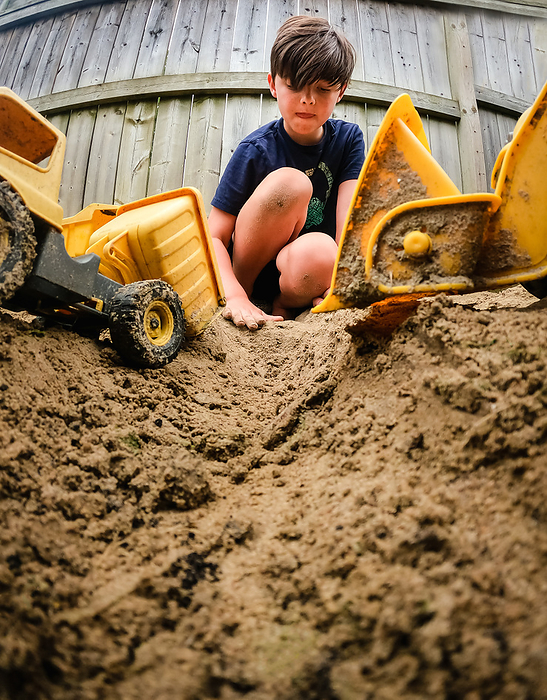 Low angle image of young boy playing with trucks in a sandbox.