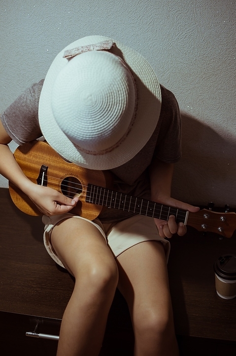 Girl in straw hat and shorts, playing ukulele bent over