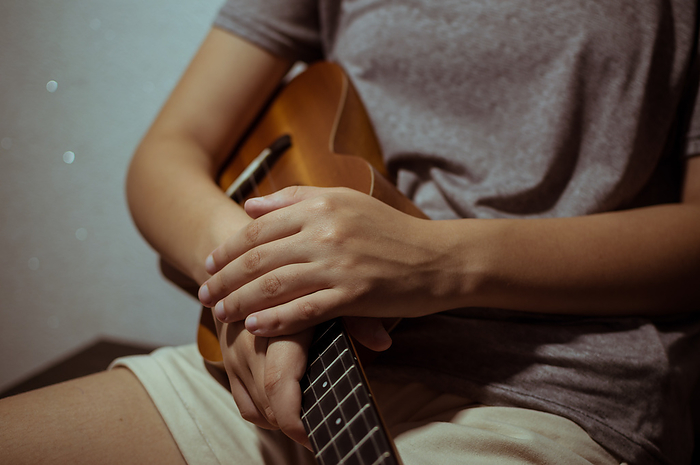 Girl's hands folded on wooden ukulele, close-up