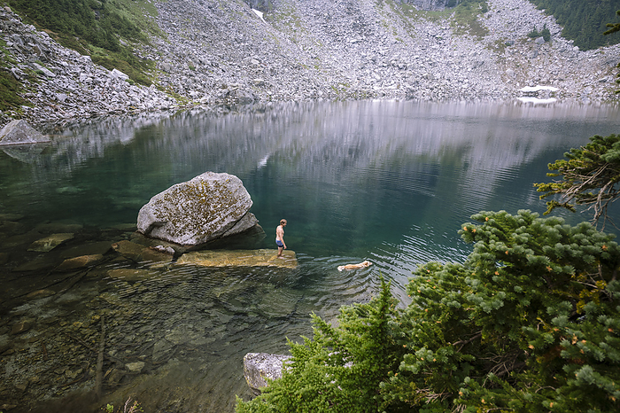 Male hiker and dog swimming in a turquoise alpine lake