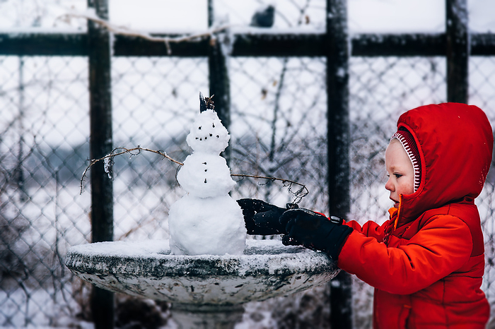 Boy building a snowman in a red coat