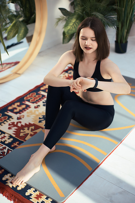 Young woman in sportswear presses on smart bracelet at home