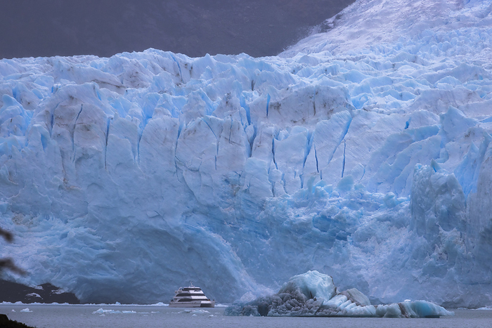 cracks and blues in the front of a glacier with a ship in foreground