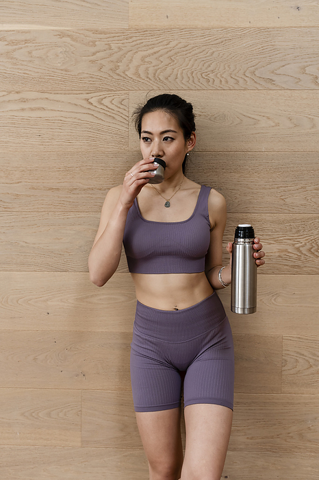 Asian woman in workout tight suit is holding yoga tea before workout