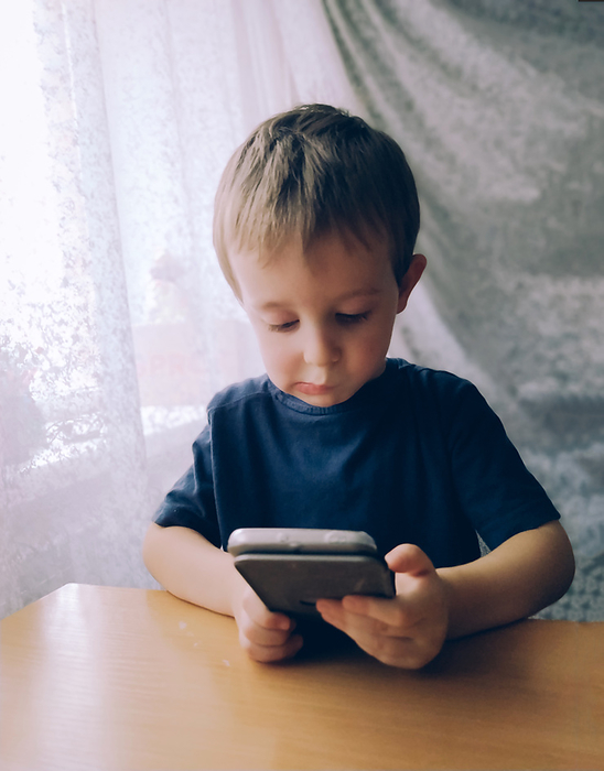 Little boy thoughtfully looks into a smartphone at a table indoors