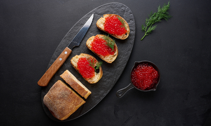 Red caviar on slices of white wheat bread on a black table, concept of luxury and gourmet cuisine Red caviar on slices of white wheat bread on a black table, concept of luxury and gourmet cuisine