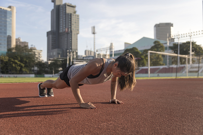 Young woman practicing push ups at sports field