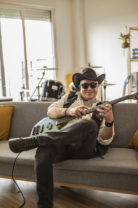 Smiling guitarist wearing hat and practicing guitar at home