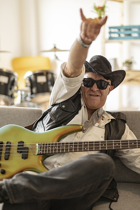 Happy guitarist wearing hat and gesturing horn sign at home