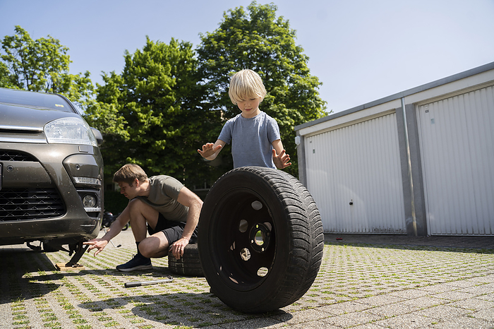 Boy helping father changing car tire in yard