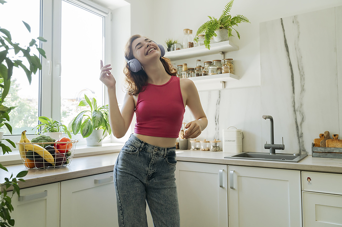 Happy young woman wearing wireless headphones listening to music and dancing at home