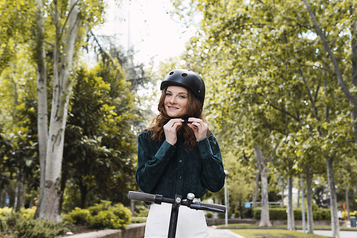Happy young woman adjusting helmet in park
