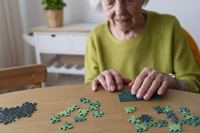 Senior woman solving jigsaw puzzle on table at home