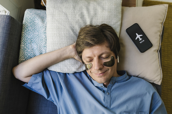 Smiling man with eye patch sleeping next to smart phone on bed at home