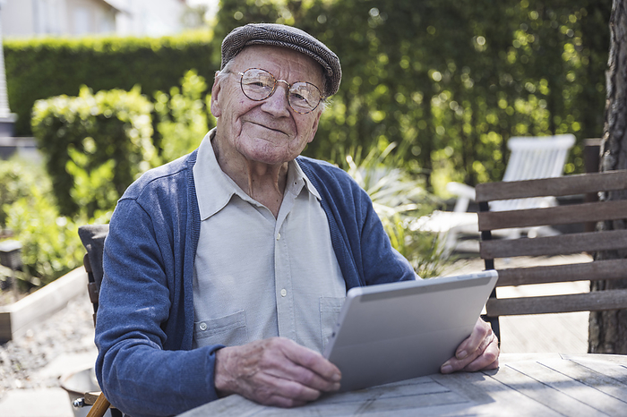 Smiling senior man sitting with tablet PC at table in back yard