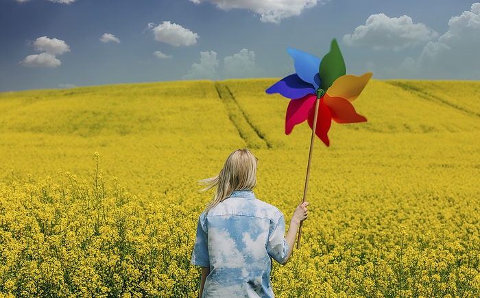 Woman holding colorful pinwheel toy in rapeseed field