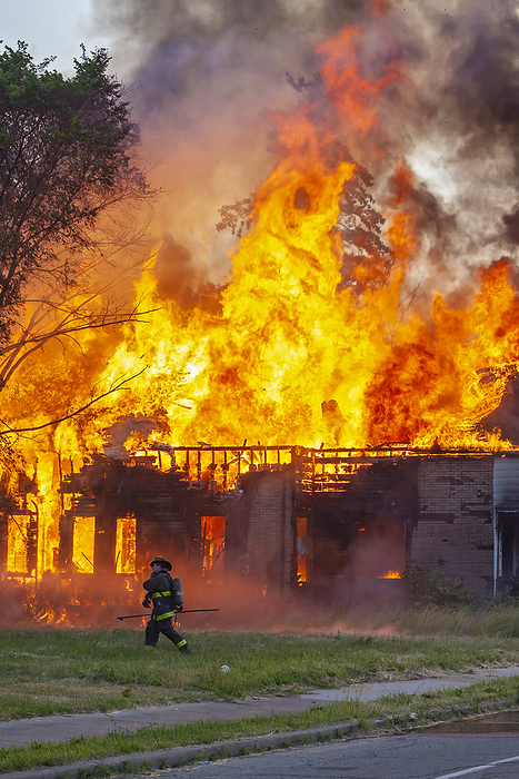 Firefighters tackling house fire Abandoned house burning from a suspected arson attack with a firefighter at the scene. Photographed in Detroit, Michigan, USA., by JIM WEST SCIENCE PHOTO LIBRARY
