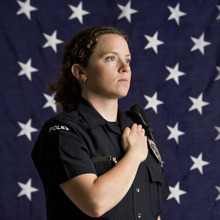 Portrait of mid adult Caucasian policewoman pledging allegiance with American flag as backdrop.