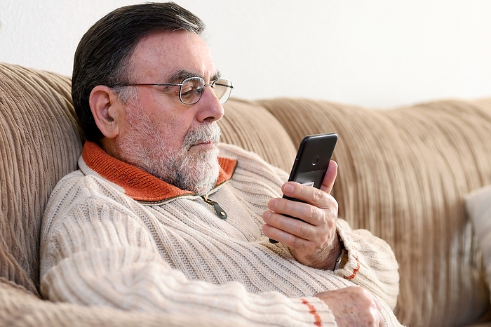 Elderly Man Using Cellphone Sitting On Sofa At Home, during Coronavirus quarantine. Elderly Man Using Cellphone Sitting on Sofa at Home, During Coronavirus Quarantine., by Zoonar DAVID HERRAEZ