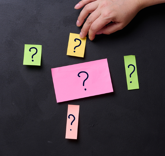 A hand sticks a sticker with question marks onto a board, representing the concept of searching for solutions and answers to questions A hand sticks a sticker with question marks onto a board, representing the concept of searching for solutions and answers to questions
