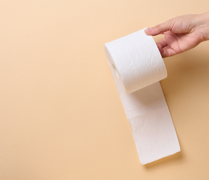 A female hand holds a roll of white toilet paper against a beige background A female hand holds a roll of white toilet paper against a beige background