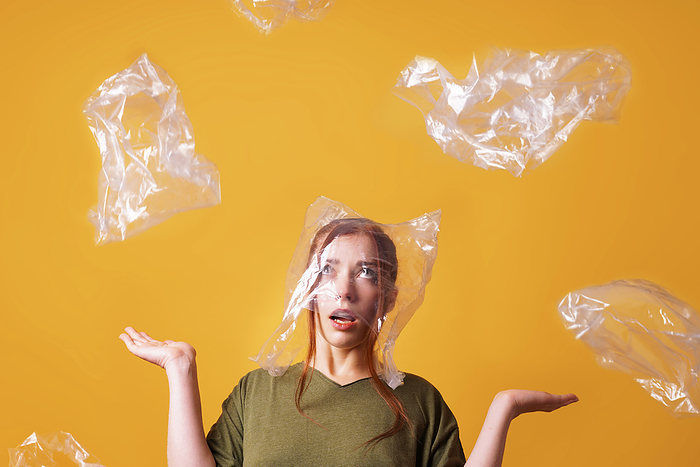 woman overwhelmed by plastic waste and suffocating from plastic bag over her head - ecology and pollution concept