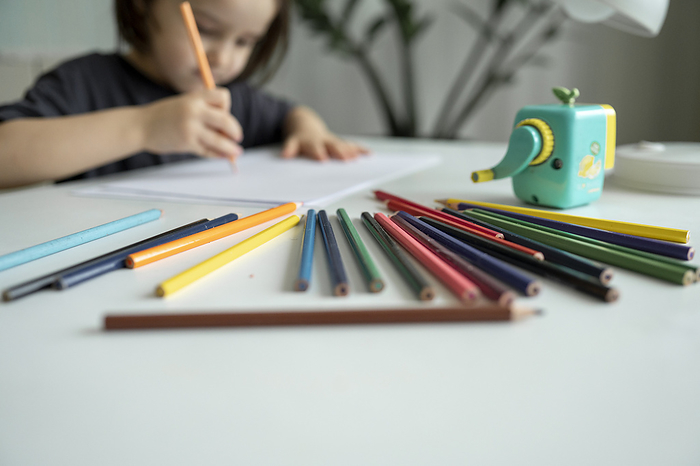 Boy drawing with colored pencils on table at home