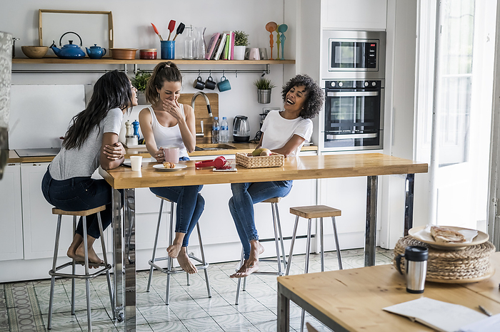 Three happy women sitting at kitchen table at home socializing