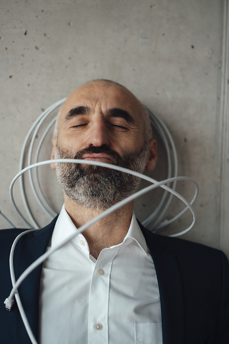 Mature businessman with computer cable leaning on wall