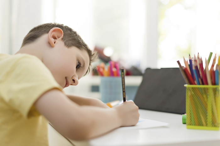 Boy in concentration learning to draw with colored pencil at home