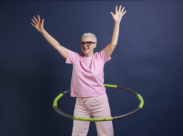 Senior woman practicing hula hoop against blue background