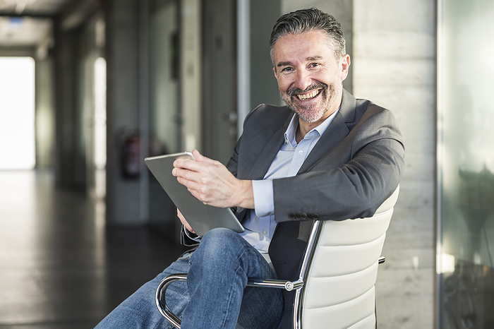 Portrait of a happy mature businessman with tablet sitting on chair in office