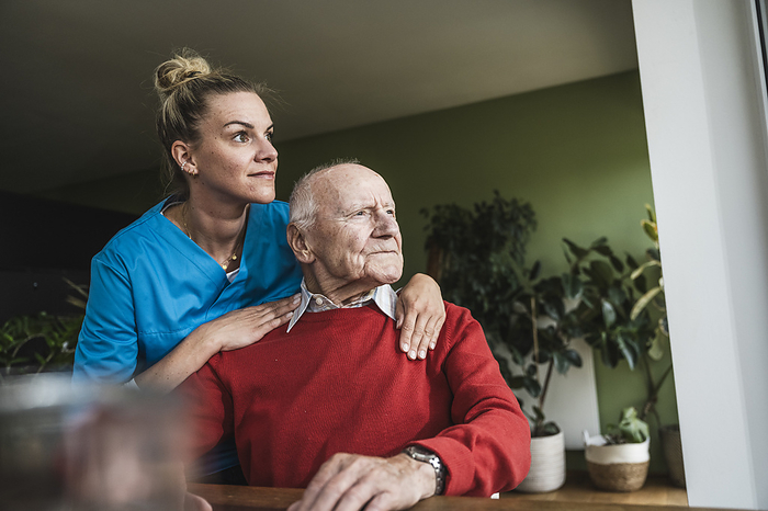 Smiling nurse with thoughtful senior man sitting at home