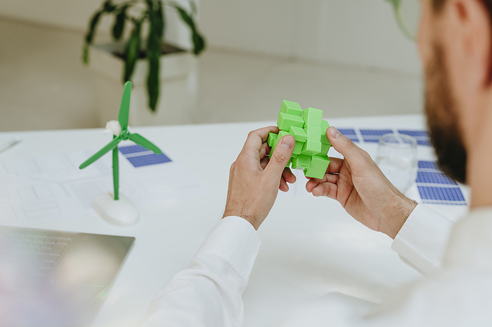 Businessman solving green puzzle cube at desk