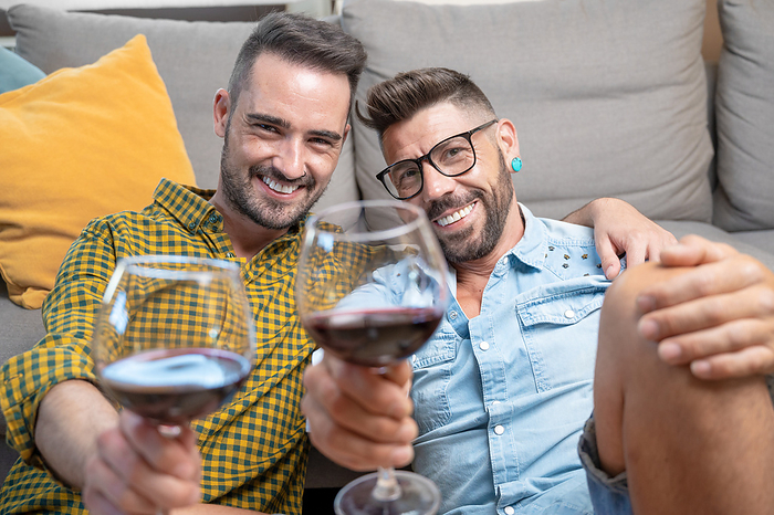 Gay couple in love sitting at home on the floor and toasting with red wine. Gay couple in love sitting at home on the floor and toasting with red wine., by Zoonar DAVID HERRAEZ