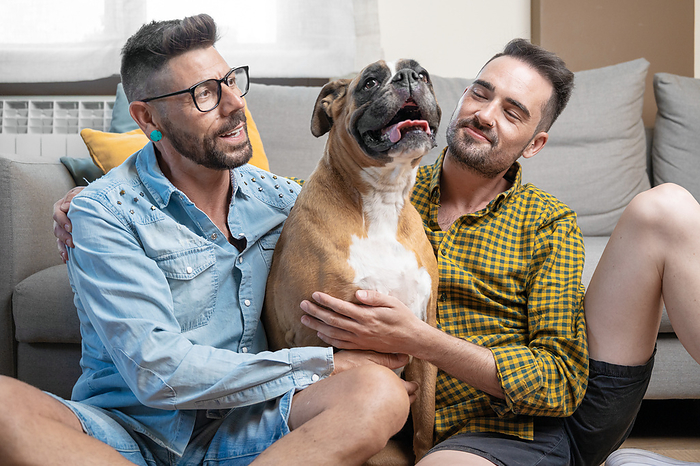 Happy gay couple sitting on floor and playing with dog at home Happy gay couple sitting on floor and playing with dog at home, by Zoonar DAVID HERRAEZ