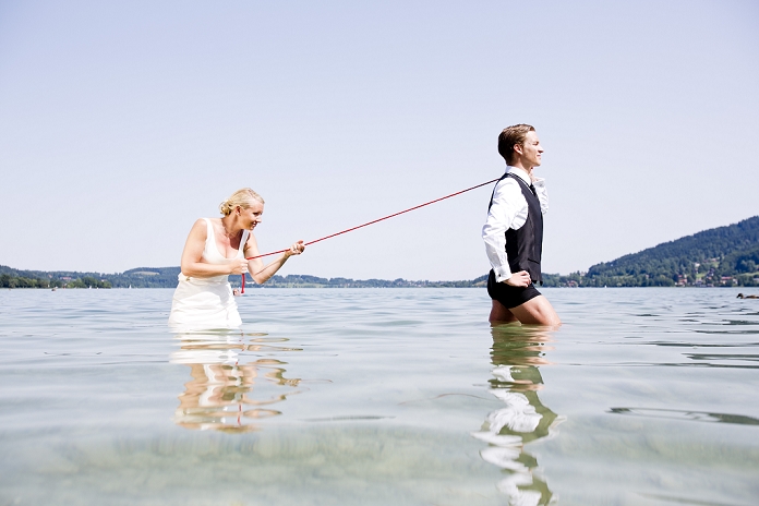 Germany, Bavaria, Tegernsee, Wedding couple standing in lake, bride holding groom on leash