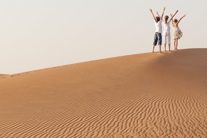 Children standing in desert with arms raised in air
