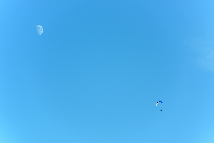 Paramotor in flight on a sunny day with the moon in the sky. Paramotor in flight on a sunny day with the moon in the sky., by Zoonar christian d 