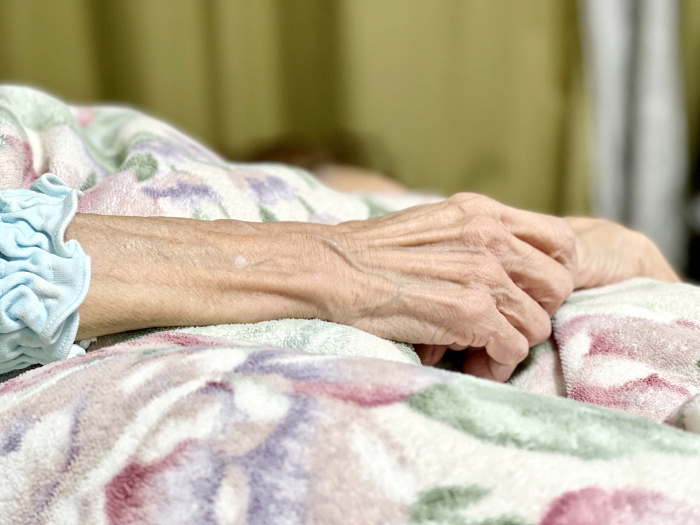 Elderly hand sleeping on a flower-patterned comforter.