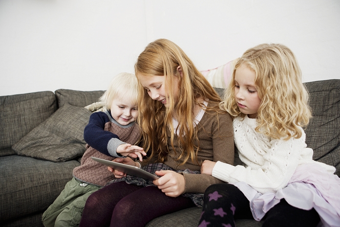 Children using tablet computer on sofa