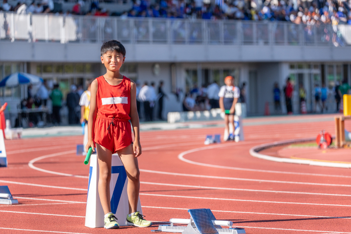 Elementary school boy running a relay at a track meet.