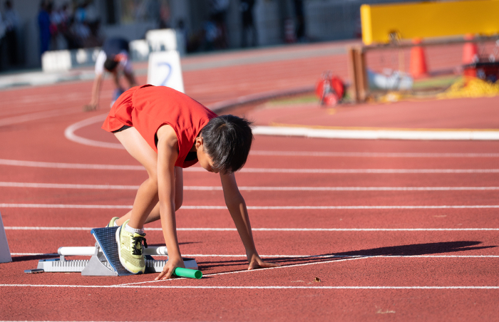 Elementary school boy running a relay at a track meet.