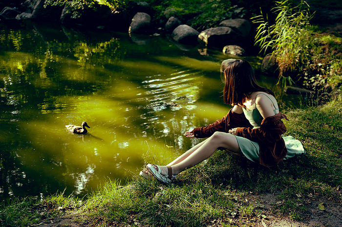 A girl in a mint dress by the lake feeds a duck from her hand, by Cavan Images / Inna Maksymenko