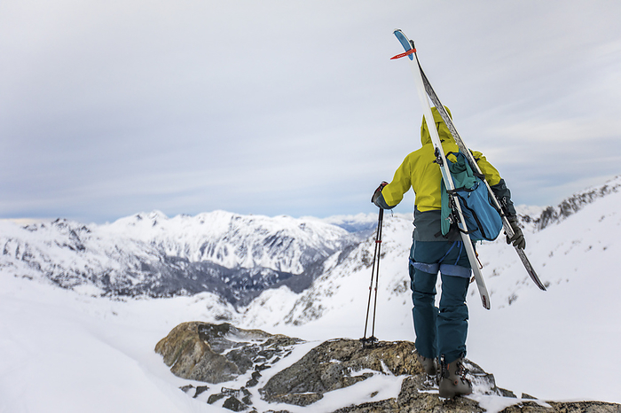 standing on mountain summit holding skis, poles and backpack, by Cavan Images / Christopher Kimmel / Alpine Edge Photography