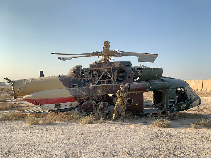 strong and manly air force man in uniform stands in front of broken down helicopter in the hot desert sun while on deployment military man stands in front of crashed helicopter in desert, by Cavan Images   Virginia Schultz