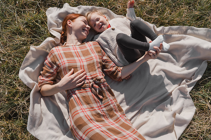 Redhead woman and her baby daughter lie in the field and laugh, by Cavan Images / Liza Zavialova