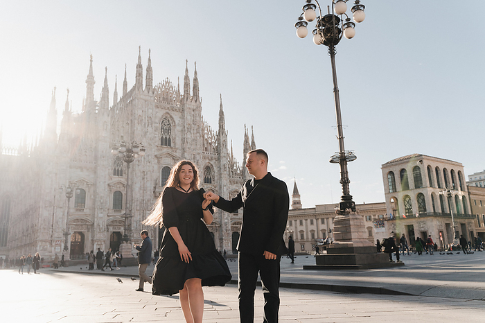 A man and a woman hold hands and walk along the Duomo square in Milan, by Cavan Images / Liza Zavialova